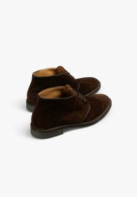 Botas desérticas de ante marrón con un diseño de cordones, forro de cuero suave y suelas de goma. Presentan una puntera redonda y una altura media en el tobillo.