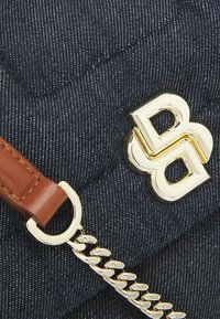 Marineblaue, gesteppte Stoffhandtasche mit einem goldenen Logo und Hardware. Sie verfügt über einen braunen Ledergriff und einen silbernen Kettenakzent.