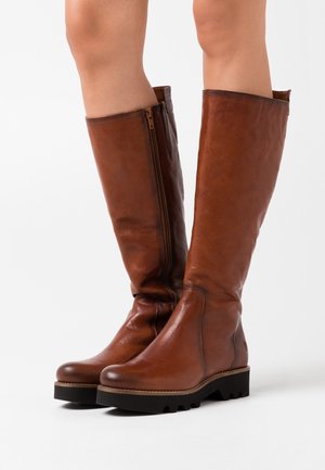 Hnědé kožené kozačky se zipem na boku, zaoblenou špičkou, texturovaným povrchem a gumovou podrážkou s viditelnými vzory terénu.