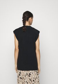 Svart ärmlös topp med subtila axelvaddar, texturerat tyg och avslappnad passform, i kombination med en mönstrad beige kjol.