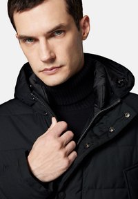 Czarna puchowa kurtka z kapturem, z zapięciem na zamek i napy. Pod spód gładki, czarny golf z żeberkowym splotem, o minimalistycznym designie.