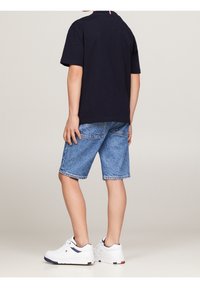 Námořnické bavlněné tričko, modré denimové šortky, bílé sportovní tenisky s barevnými akcenty; ležérní dětský outfit z pohledu zezadu.