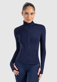 Chaqueta navy de cremallera completa fabricada en un tejido elástico, que cuenta con un cuello alto, bolsillos laterales y agujeros para los pulgares en los puños para un ajuste ceñido.