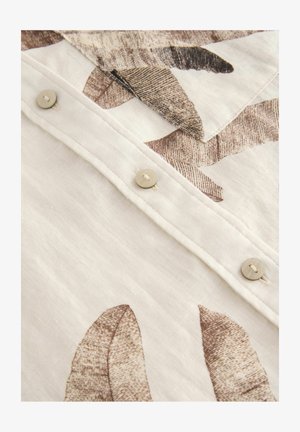 Ľanová košeľa s béžovou a hnedou potlačou listov, s krémovými gombíkmi pozdĺž predného zapínania a textúrovaným povrchom tkaniny.