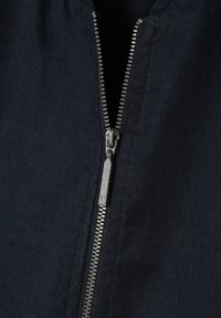 Navy látka se hladkým povrchem je opatřena kovovým zipem. Zip je umístěn centrálně a má stříbrnou táhlo, což ukazuje na funkční design.