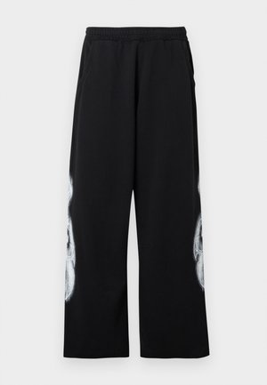 Black sweatpants with an elastic waistband, side pockets, and a large white graphic design on the outer leg. Cotton material, loose fit.