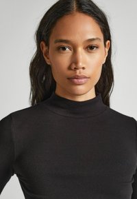 Fekete bordás, hosszú ujjú póló magas nyakkivágással; testhezálló fazon és puha tapintás. Diszkrét márkázás található a mellkason.