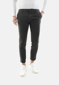 Pantaloni neri in cotone a vestibilità slim, con tasche laterali e risvolti, abbinati a sneakers bianche. Texture liscia, design minimal.