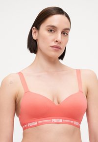 Coral bralette featuring a smooth fabric, adjustable straps, and a branded elastic band with white logo detailing.