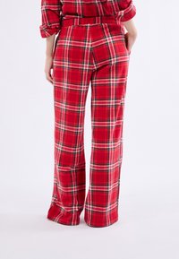 Pantaloni a quadri rossi con una vestibilità ampia, caratterizzati da un design a gamba svasata e una vita elasticizzata. Il tessuto ha un aspetto morbido e texture.