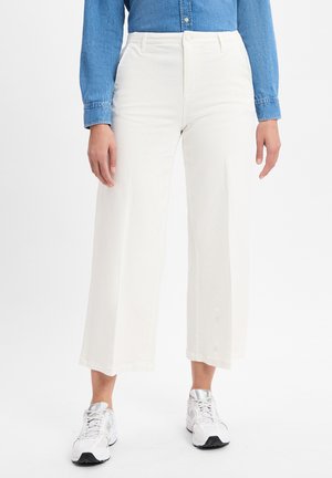 Witte wijde broek van zachte stof, met een hoge taille, voorkruiszakken en een nette afwerking. Gecombineerd met witte sportschoenen.