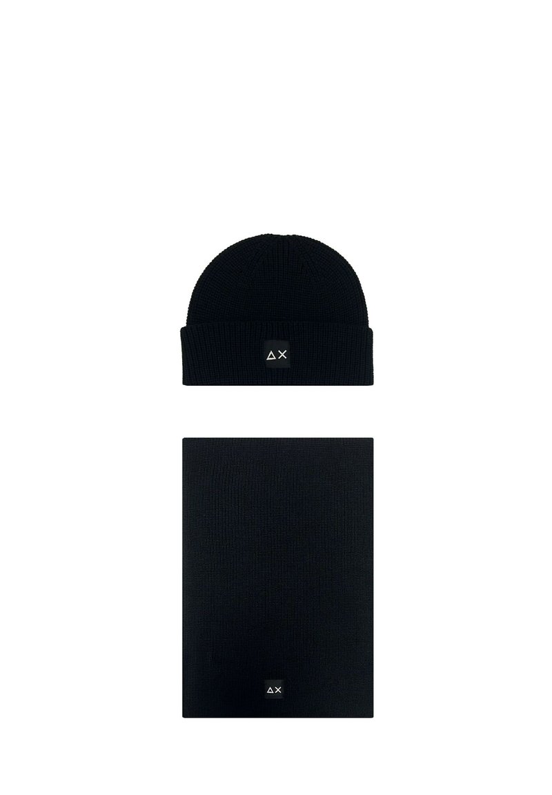 Berretto di maglia nero e sciarpa rettangolare abbinata, ciascuno con una piccola toppa nera che mostra simboli bianchi a forma di triangolo e "X".