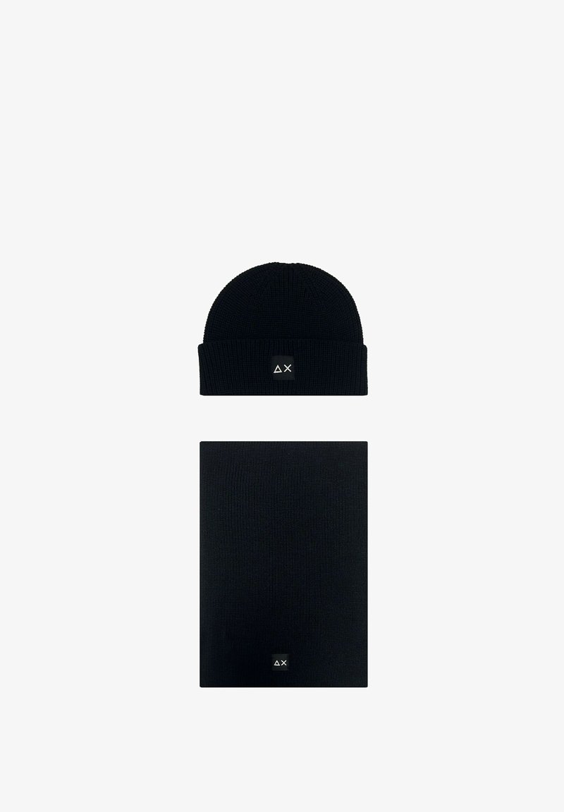 Berretto di maglia nero e sciarpa rettangolare abbinata, ciascuno con una piccola toppa nera che mostra simboli bianchi a forma di triangolo e "X".