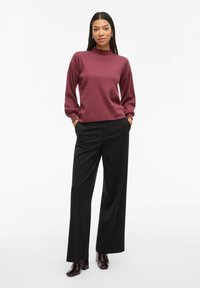 Bordeaux pullover met een hoge halslijn, ballonmouwen en geribbelde manchetten, gecombineerd met zwarte wijde broek en glanzende bordeaux enkellaarsjes.