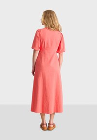 Korallenfarbenes Leinen-Midi-Kleid mit kurzen Puffärmeln, einem taillierten Oberteil und einem fließenden Rock; kombiniert mit braunen Sandalen mit einer Schnalle.