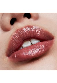 Gros plan sur des lèvres d'une couleur rose pâle et brillante. La texture semble lisse avec des plis naturels, laissant entrevoir un léger écart entre les dents.
