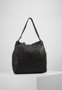 Svart läderhandväska med en avslappnad design, slät textur och ett enda axelband. Har minimal hårdvara och en välstrukturerad botten.