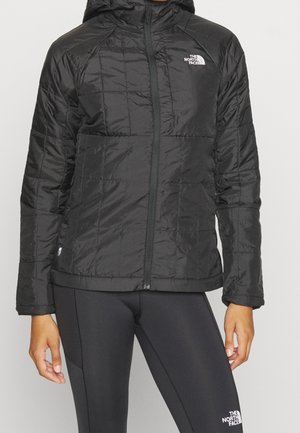 Czarna pikowana kurtka z kapturem i zamkiem błyskawicznym, noszona z czarnymi legginsami, oba z logo The North Face.