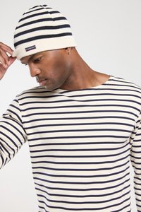 Strikket hue med striber i creme og marineblå med en foldet kant. Modellen har en matchende langærmet stribet skjorte på, der har vandrette marineblå striber.