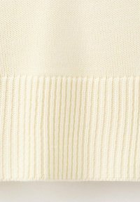 Suéter de punto en color crema claro con dobladillo acanalado y textura suave, con puntadas distribuidas uniformemente que crean un patrón sutil.