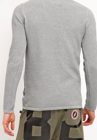 Grijze gestructureerde trui met lange mouwen, met een aansluitend ontwerp en een zijnaaddetail, gecombineerd met olijfgroene shorts en een patch.