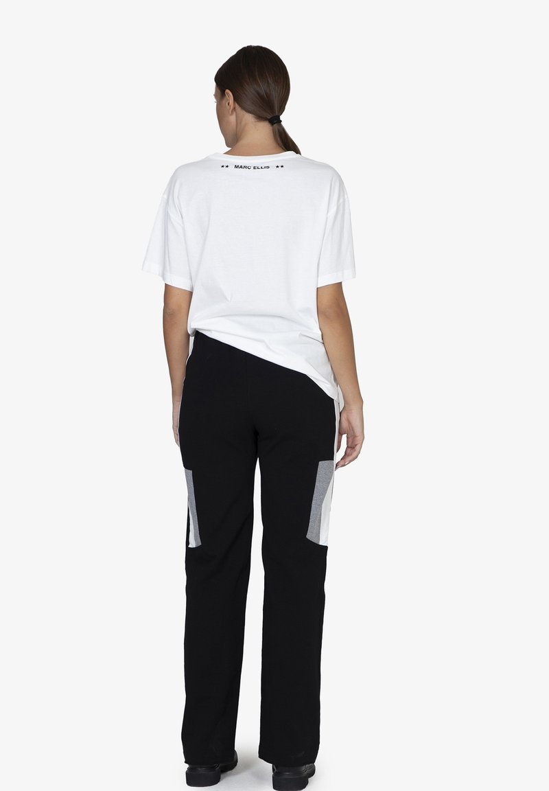 Witte katoenen T-shirt met een geprint label op de achterkant, gecombineerd met zwarte broek met grijze paneelaccenten aan de zijkanten.