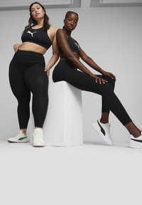 Fekete sportos crop toppok és leggings fehér és zöld sneaker cipőkkel, semleges háttér előtt bemutatva.