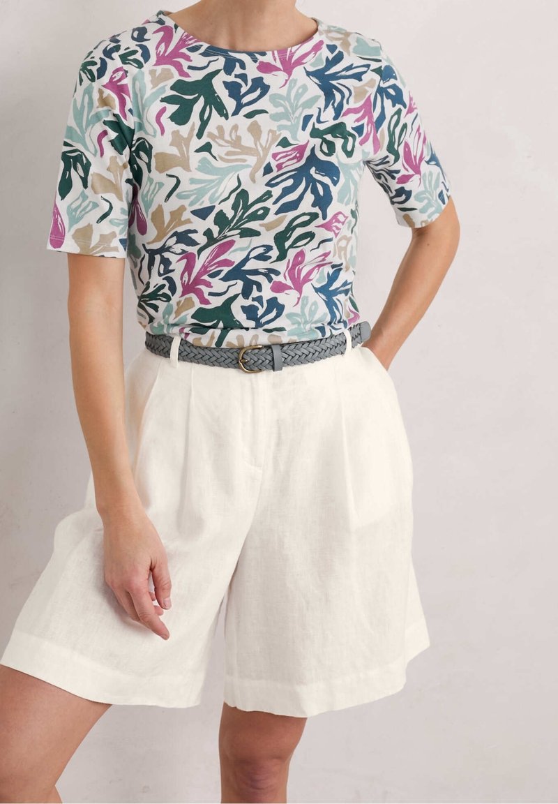 T-shirt à manches courtes de couleur bleu clair avec un motif de feuilles abstrait multicolore, associé à un short en lin blanc et une ceinture tissée grise.