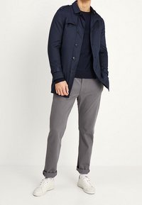 Lehký námořnický trenčkot přes tmavý svetr, doplněný světlými šedými kalhotami a bílými teniskami. Má zapínání na knoflíky vpředu a ohrnuté manžety.