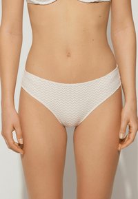 Białe spodnie bikini z teksturowanym, plecionym wzorem. Projekt ma średni stan i gładkie krawędzie dla wygody.