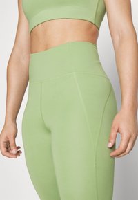 Legginsy sportowe o wysokim stanie w jasnym zielonym kolorze, wykonane z elastycznego materiału z płaskimi szwami i gładką teksturą, zaprojektowane z myślą o komforcie i elastyczności.