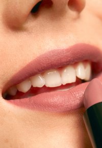 Matt rosa läppstift är applicerat på läpparna, vilket framhäver en jämn textur. Läpparna är fylliga, med synliga vita tänder och subtila konturer.