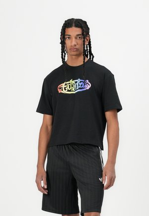 Black cropped t-shirt featuring a multicolored "adidas" logo in a playful font. Paired with black shorts displaying subtle vertical stripes.