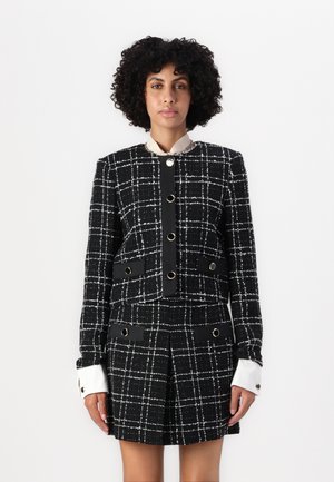 Black and white checkered blazer with a structured design, featuring gold-tone hardware and contrasting white cuffs. Textured fabric with pockets.