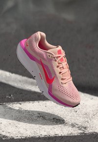 Lichtroze Nike hardloopschoen met een ademende mesh bovenkant, roze accenten en een witte rubberen zool met een subtiel textuurpatroon.