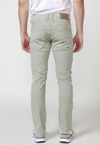 Jeans verde claro, ajustados al cuerpo, con bolsillos traseros, trabillas para el cinturón y una etiqueta de cuero marrón en la cinturilla. Textura de tela suave y lisa.