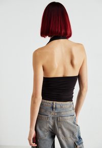 Črn top z halter krojem, ki tesno prilaga in ima gladko teksturo, v kombinaciji z visokim pasom ter bledimi modrimi denim hlačami s stranskimi žepi.