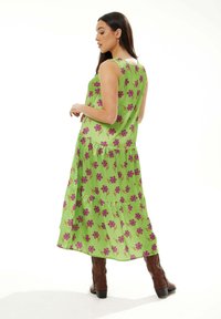 Green floral maxi dress with purple flowers, sleeveless design, tiered hem, paired with brown knee-high boots. Smooth fabric texture.