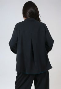 Black blazer with a smooth fabric, featuring a classic collar, back pleat detail, and relaxed fit. Suitable for various occasions.