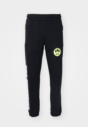 Pantalons de jogging noirs en tissu doux, avec un visage souriant néon vert et une impression graphique blanche sur le côté, avec des poignets et une taille élastiques.