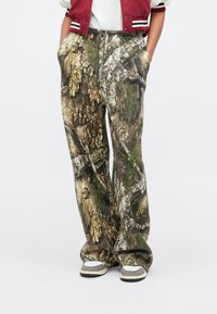 Nohavice s maskáčovým vzorom v odtieňoch hnedej, zelenej a béžovej; široký strih; elastický pás so sťahovacou šnúrkou; jemná textúra, pohodlný dizajn.