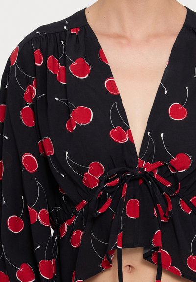 Blusa nera corta con stampa di ciliegie rosse, scollatura a V, spalle arricciate e lacci in vita. Tessuto leggero e design morbido.