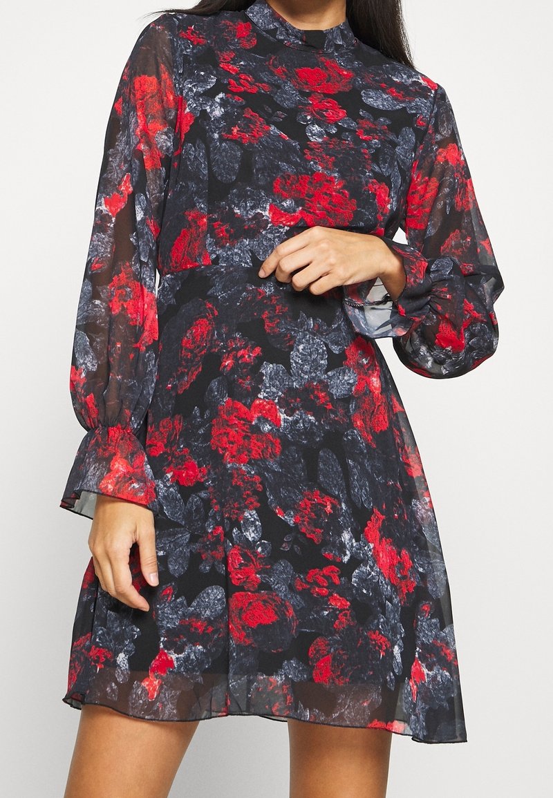 Un vestido floral con un fondo negro, patrones rojos y grises, mangas largas transparentes, un escote alto y un dobladillo acampanado.