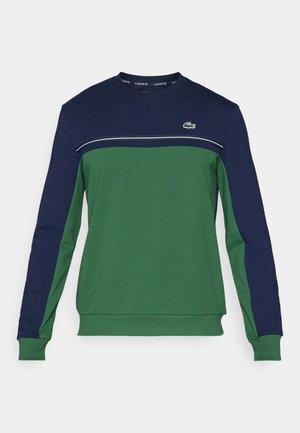 Sudadera de cuello redondo con cuerpo verde y parte superior del pecho y mangas en azul marino, que presenta finas rayas blancas y un pequeño logo bordado de cocodrilo.