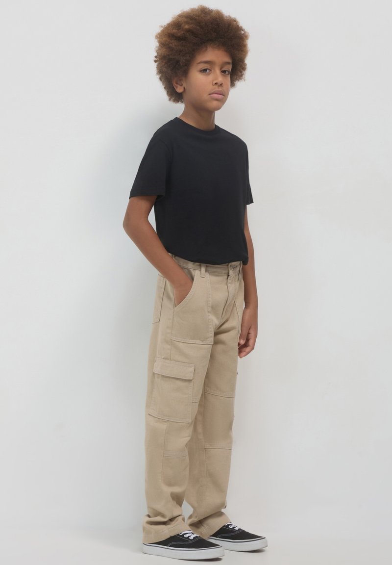 Schwarzes kurzärmliges T-Shirt kombiniert mit beigen Cargo-Hosen mit Seitentaschen, ergänzt durch schwarze Sneakers mit weißen Sohlen.