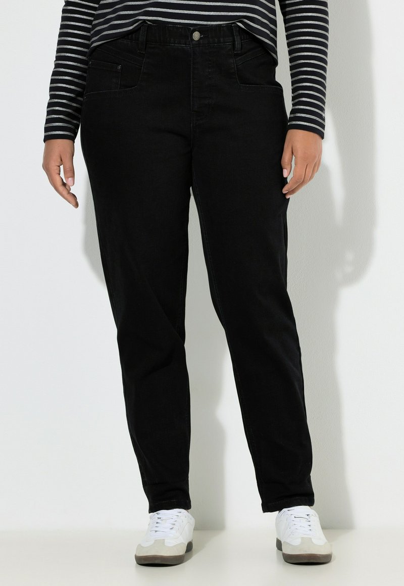 Schwarze Jeans aus Denim mit geradem Schnitt, fünf Taschen und einem Knopfverschluss. Kombiniert mit weißen Schuhen und einem gestreiften Langarmshirt.