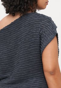 Graues, strukturiertes Oberteil mit wellenförmigem, gewelltem Design und kurzen Ärmeln. Das Material wirkt weich und leicht locker sitzend.