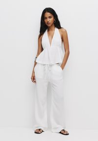 Bijela halter majica s peplum dizajnom u kombinaciji s širokim bijelim hlačama. Lagani materijal, minimalna tekstura i opušteni silueta.