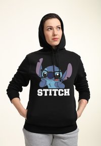 Černá mikina s kapucí, na které je grafika kreslené postavy s modrou pletí a růžovýma ušima, text "STITCH" v tučném bílém písmu ve spodní části.