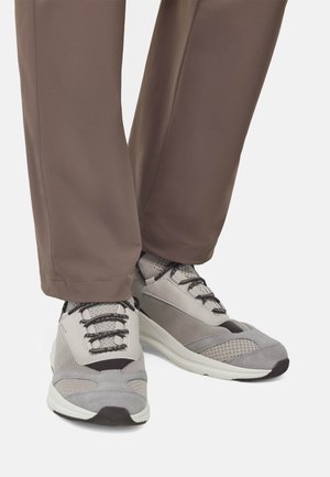 Graue Sportschuhe mit einer Kombination aus Mesh- und Wildledertexturen, runder Zehenpartie und schwarzem Schnürdesign, kombiniert mit braunen geraden Hosen.